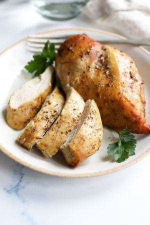 air fryer chicken breasts on white plate with 1 sliced