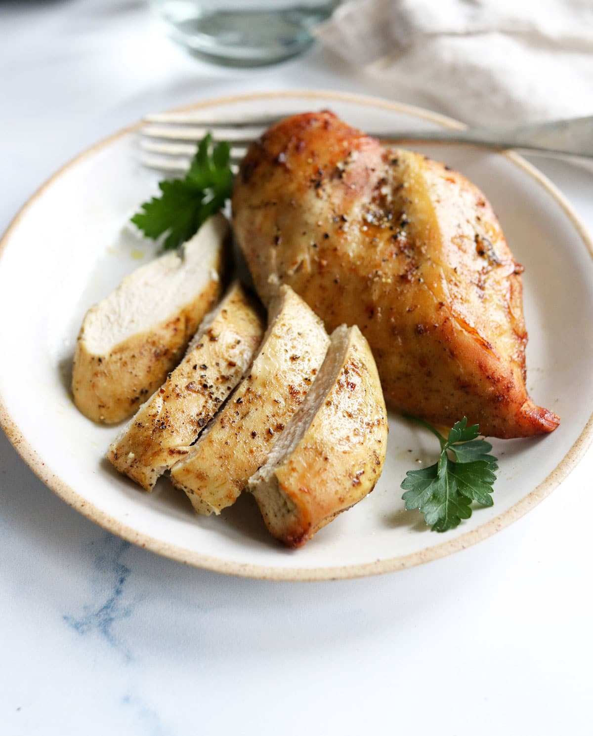 air fryer chicken breasts on white plate with 1 sliced