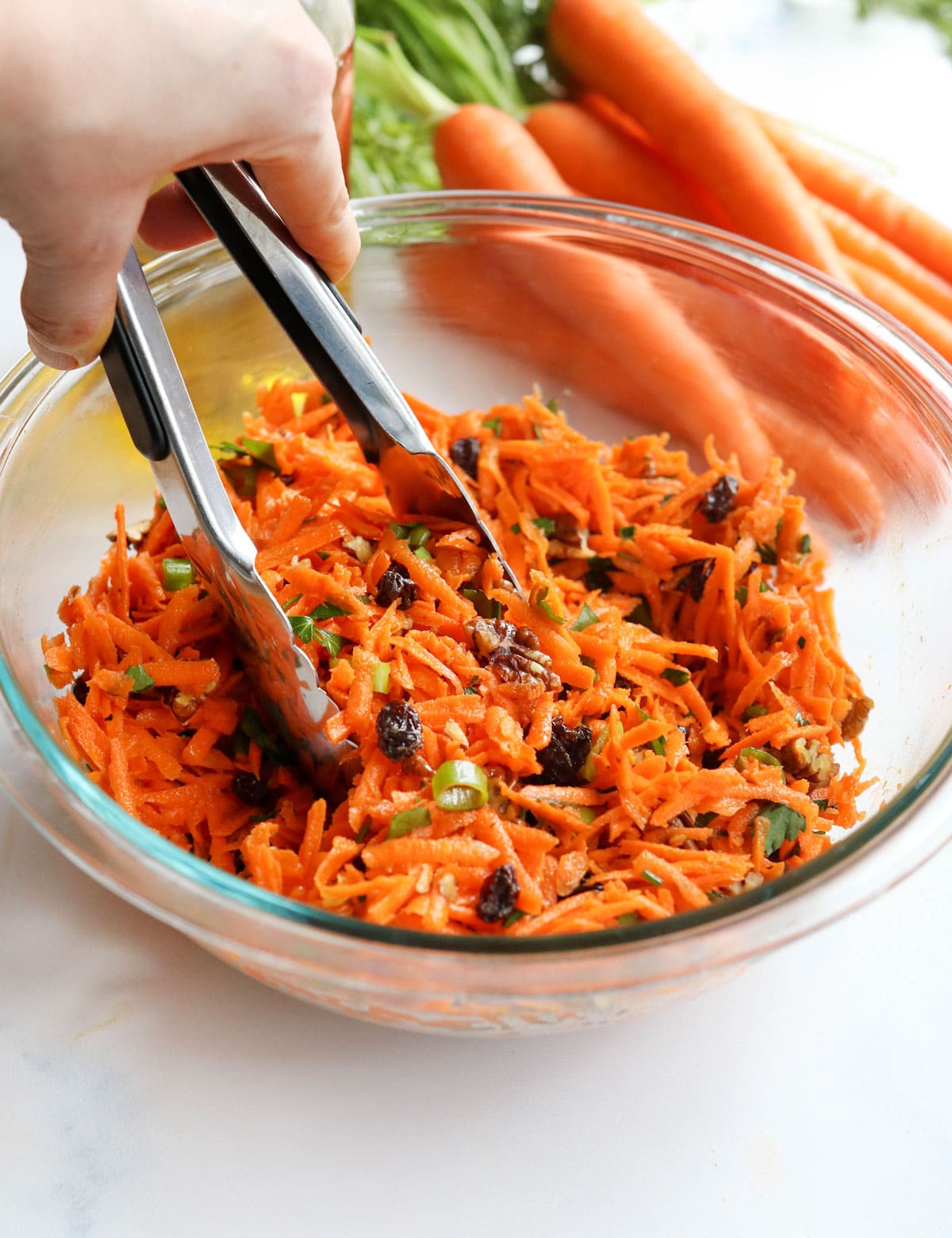 carrot salad in glass bowl with tongs