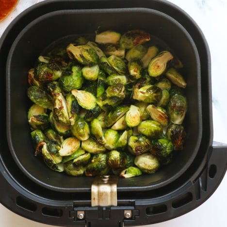 brussels sprouts in an air fryer basket near a sauce.