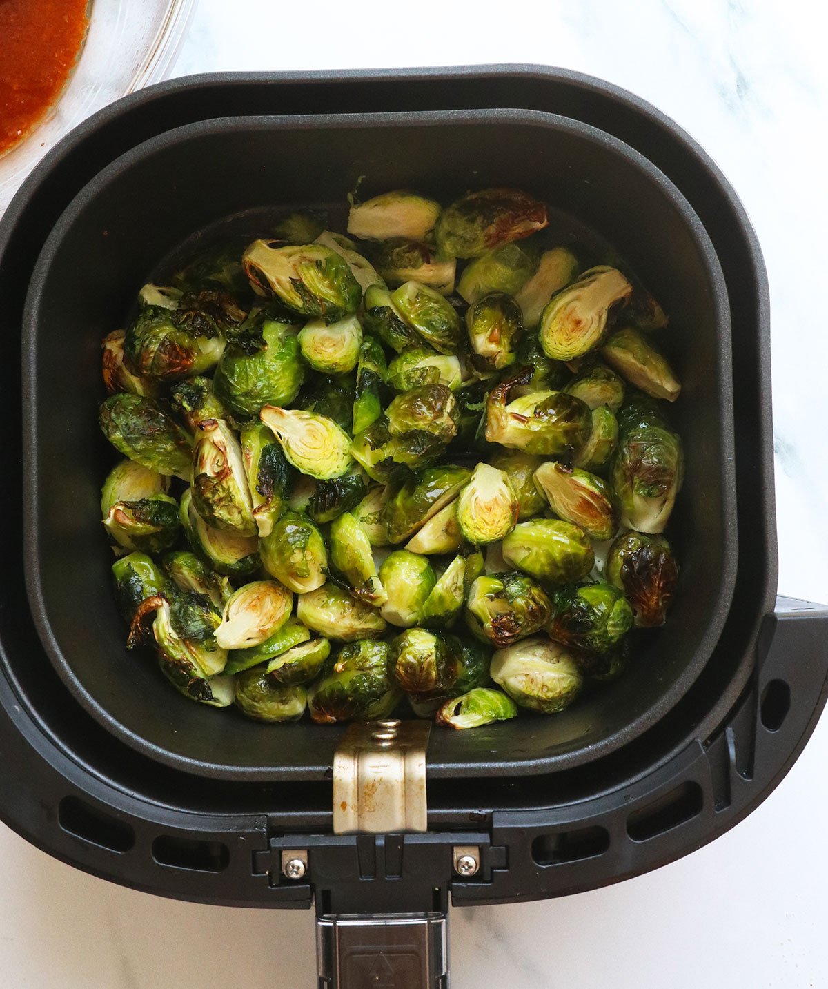 Brussels sprout in an air frying basket near the sauce.