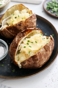 air fryer baked potatoes topped with butter and chives.