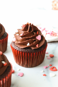 Chocolate almond flour cupcake topped with frosting and heart sprinkles.