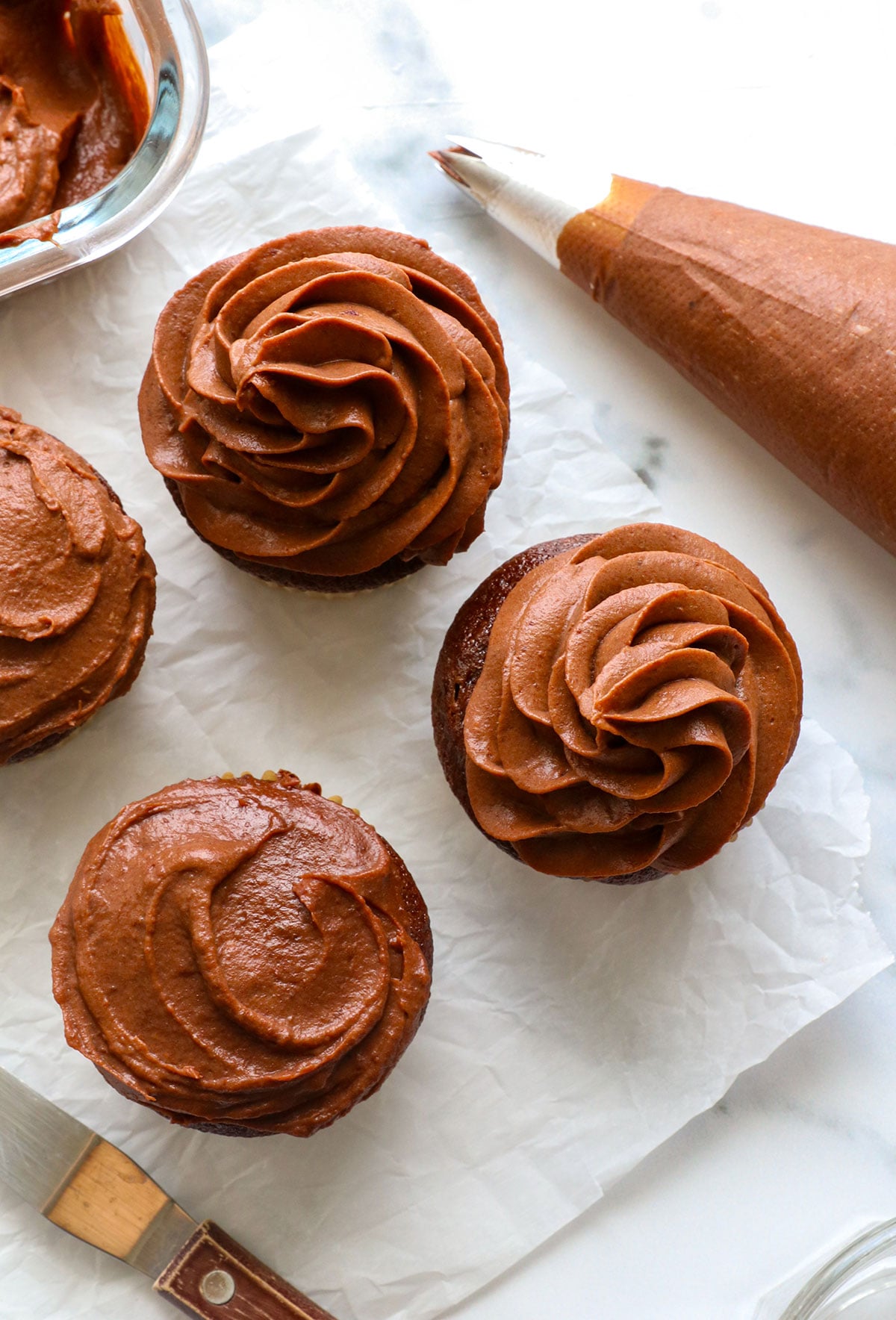 chocolate frosting without powdered sugar added to cupcakes with a piped tip and spread with a knife.