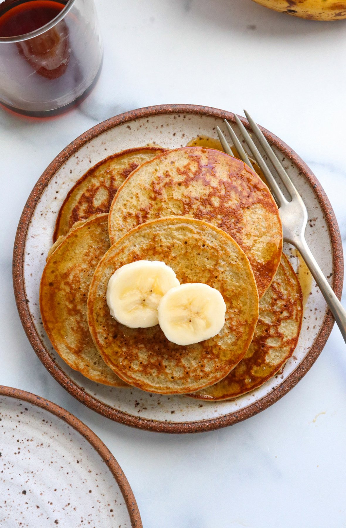 banana egg pancakes stacked on a white plate and topped with sliced banana.