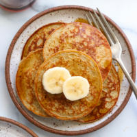 banana egg pancakes stacked on a white plate and topped with sliced banana.