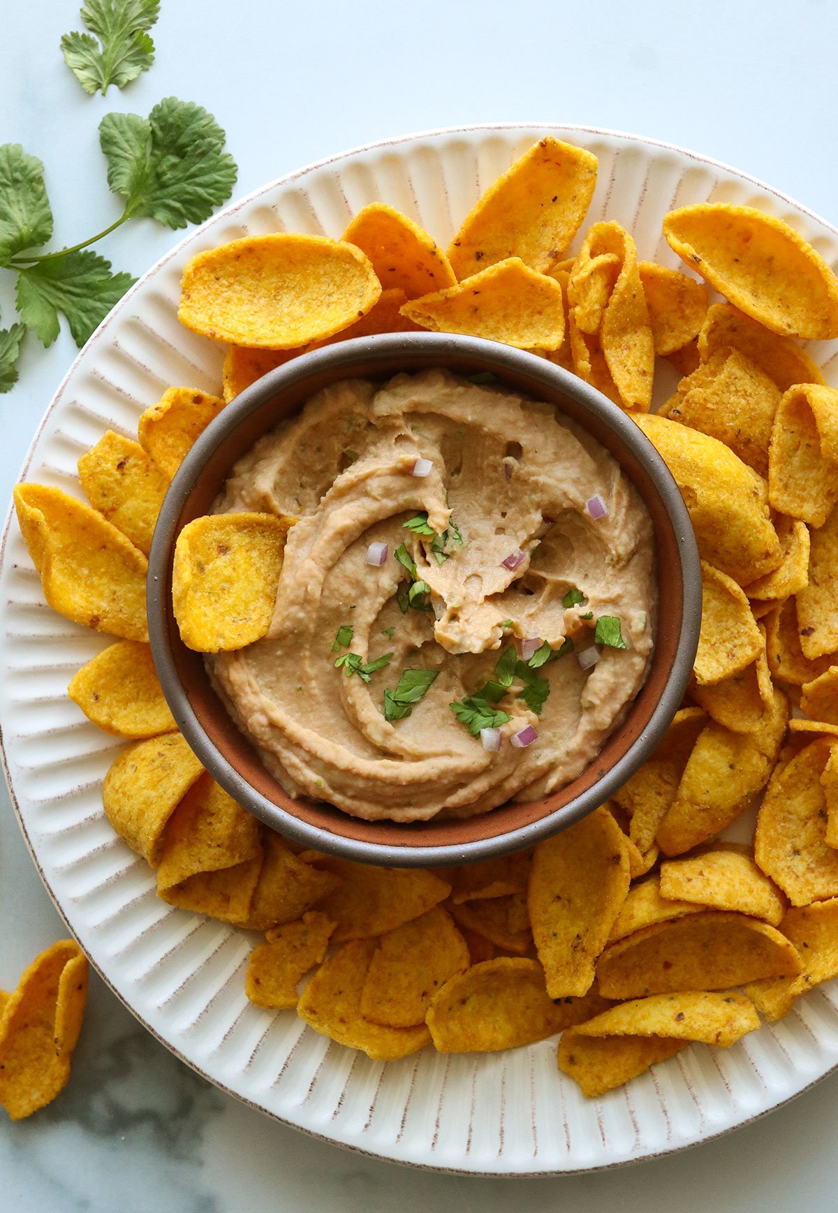 bean dip garnished with cilantro and red onion served with corn chips.