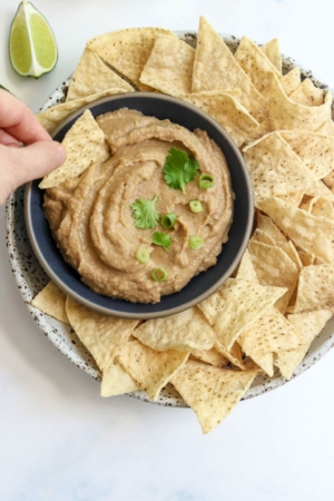 hand holding a chip, dipping it into a bowl of bean dip