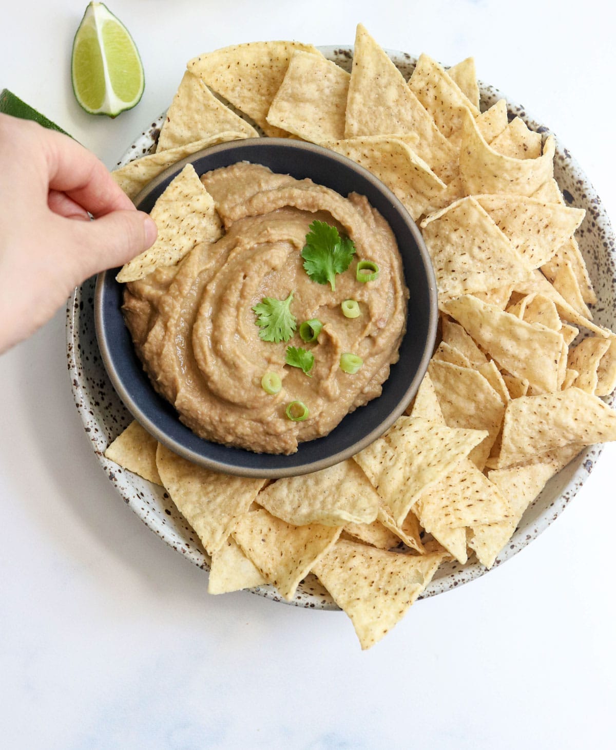 hand holding a chip, dipping it into a bowl of bean dip