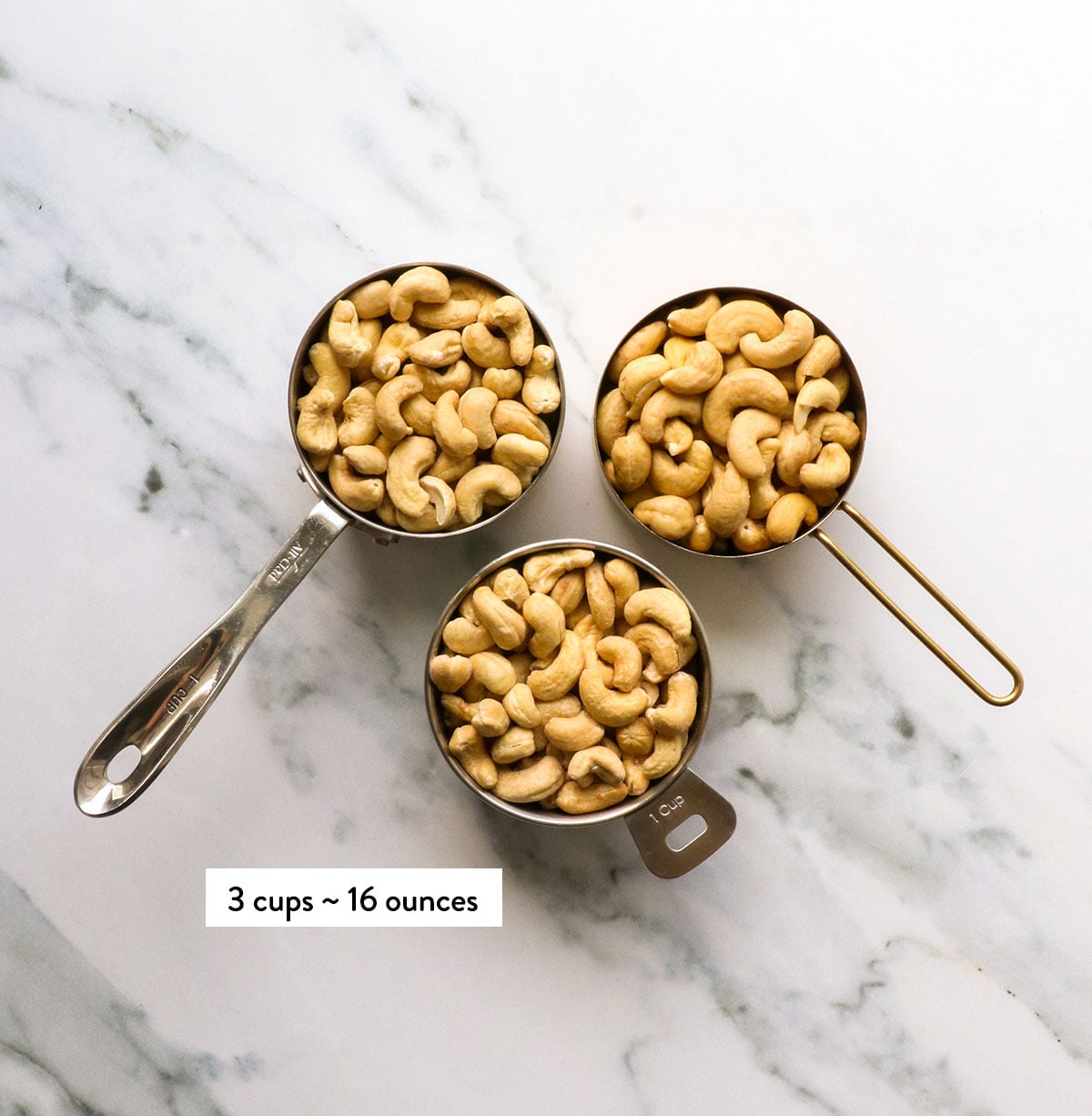 3 cups of whole cashews on a marble surface.