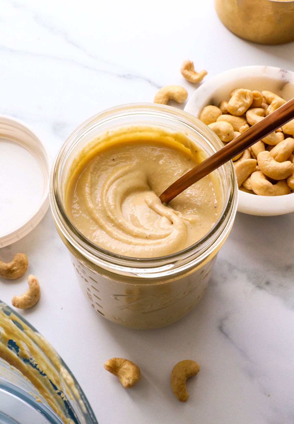 homemade cashew butter in a jar with cashews nearby.