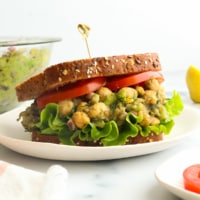 chickpea salad sandwich with sliced tomatoes and a toothpick in the bread.