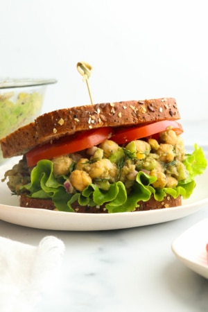 chickpea salad sandwich with sliced tomatoes and a toothpick in the bread.