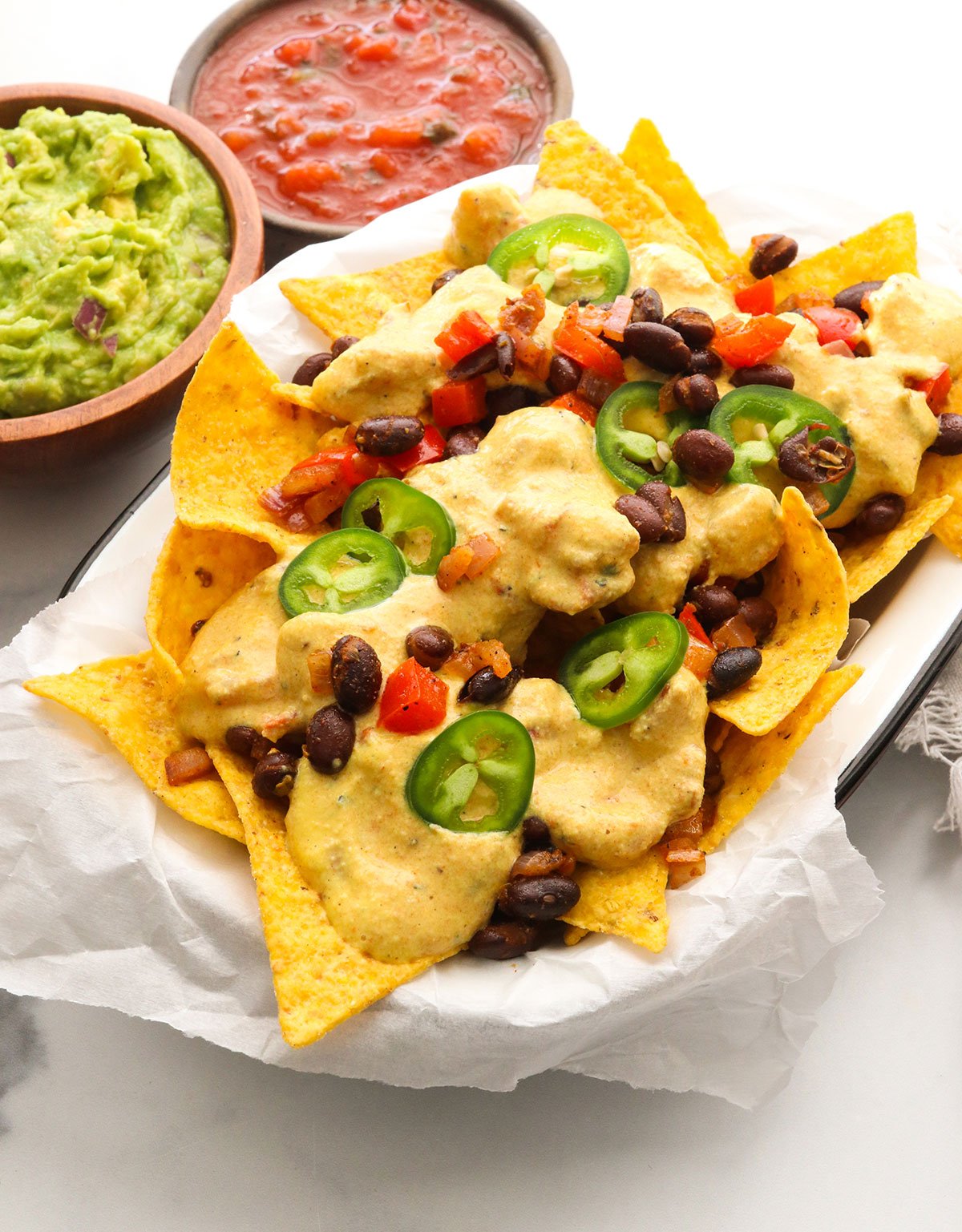 tortilla chips loaded with vegan nacho toppings and a side of guacamole and salsa.