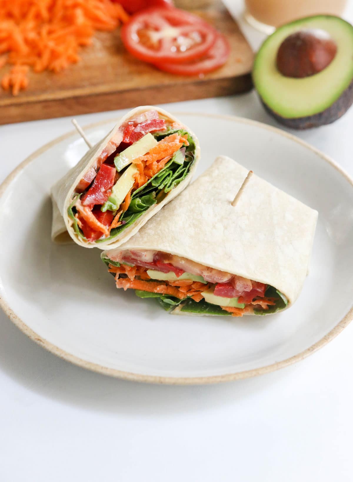 veggie wrap on a white plate with avocado behind it