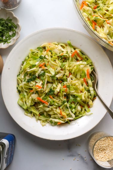 Asian slaw served in a white bowl with a fork.
