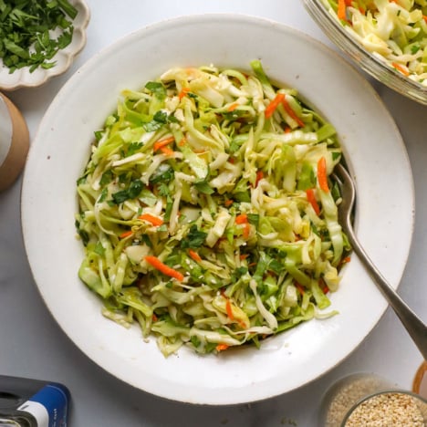Asian slaw served in a white bowl with a fork.