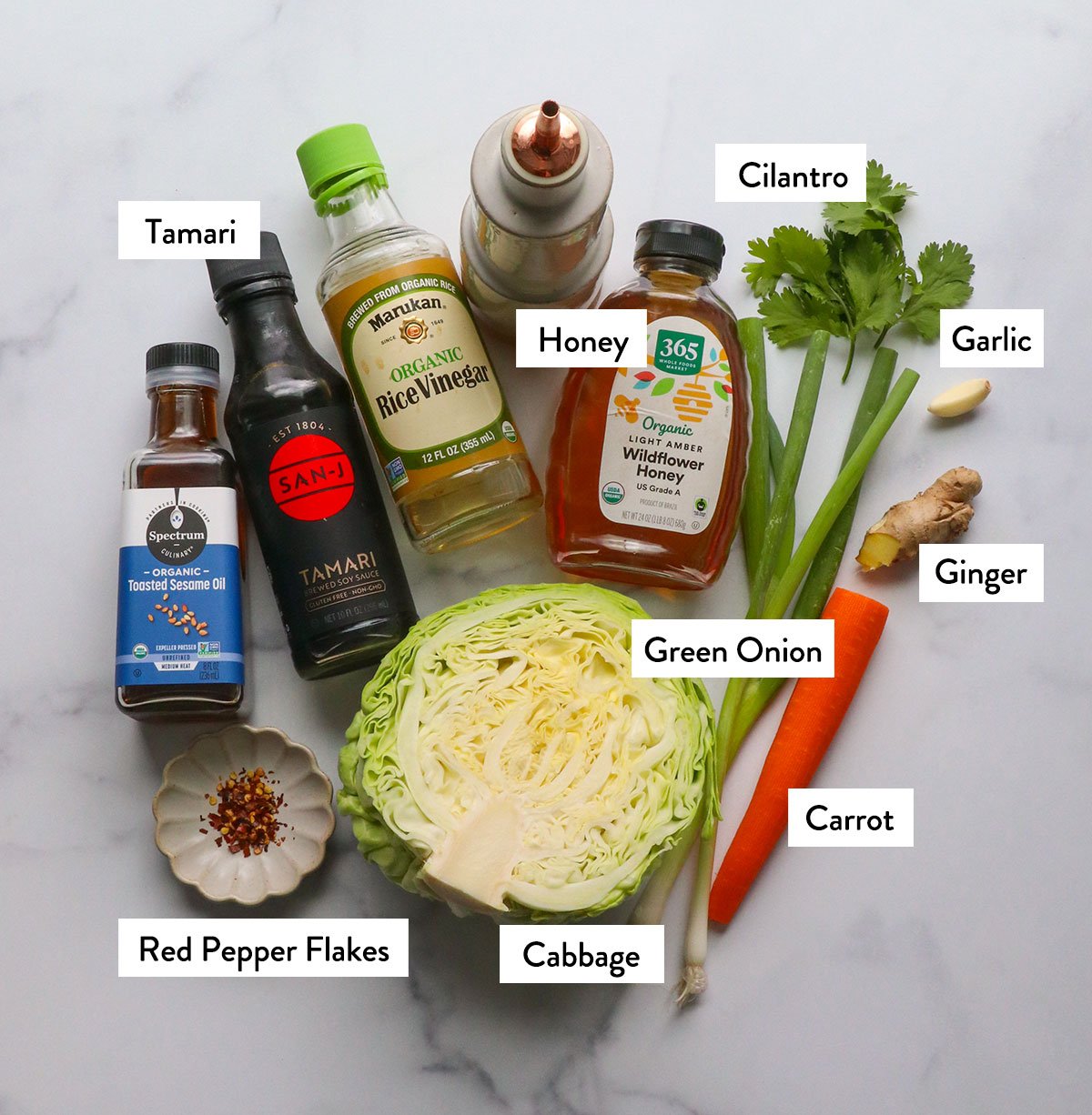 Cabbage, honey, carrots, green onions, red pepper flakes and coriander are marked with coriander on a white plate.