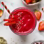beet smoothie in a glass with sliced strawberries and a striped straw.