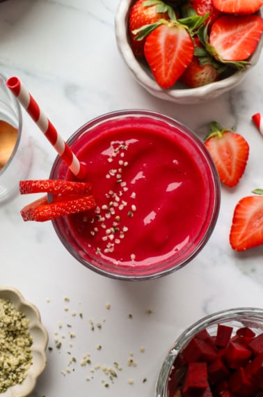 beet smoothie in a glass with sliced strawberries and a striped straw.
