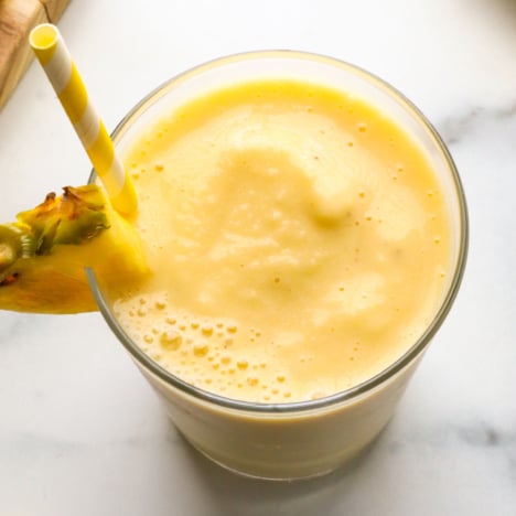 pineapple banana smoothie served with a yellow straw and pineapple wedge.