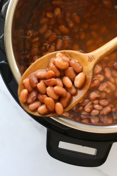 instant pot pinto beans on a spoon resting on the pot.
