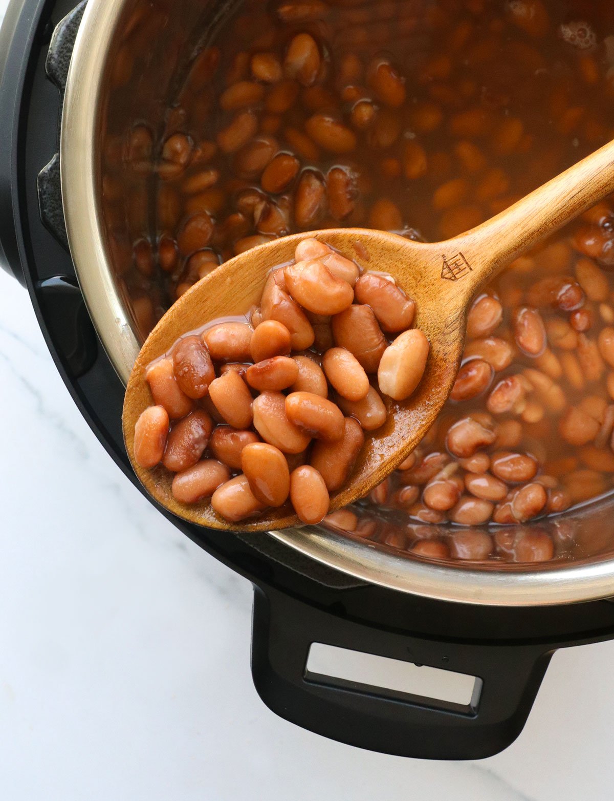 instant pot pinto beans on a spoon resting on the pot.