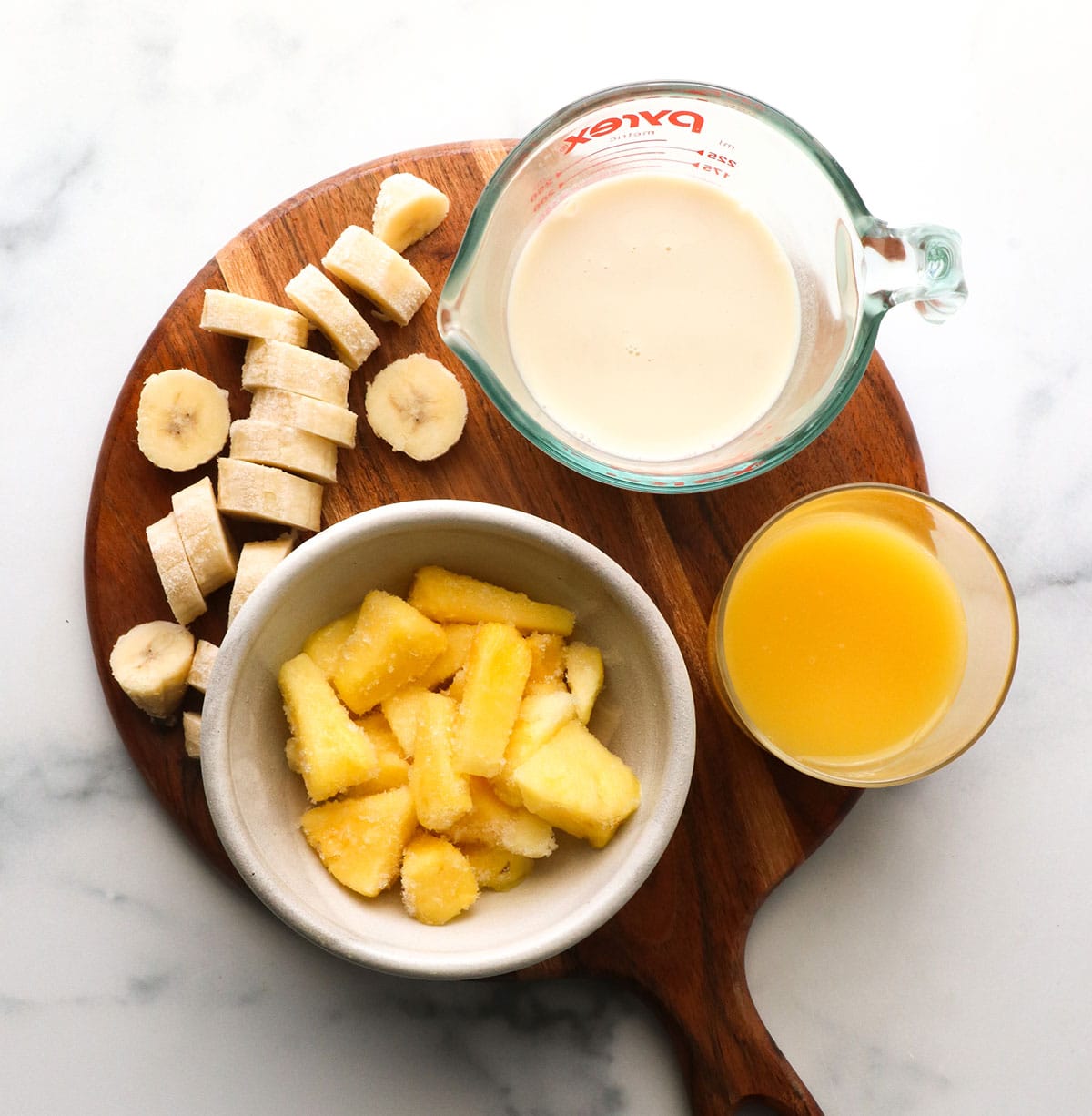 frozen pineapple, banana, milk, and OJ on a board. 