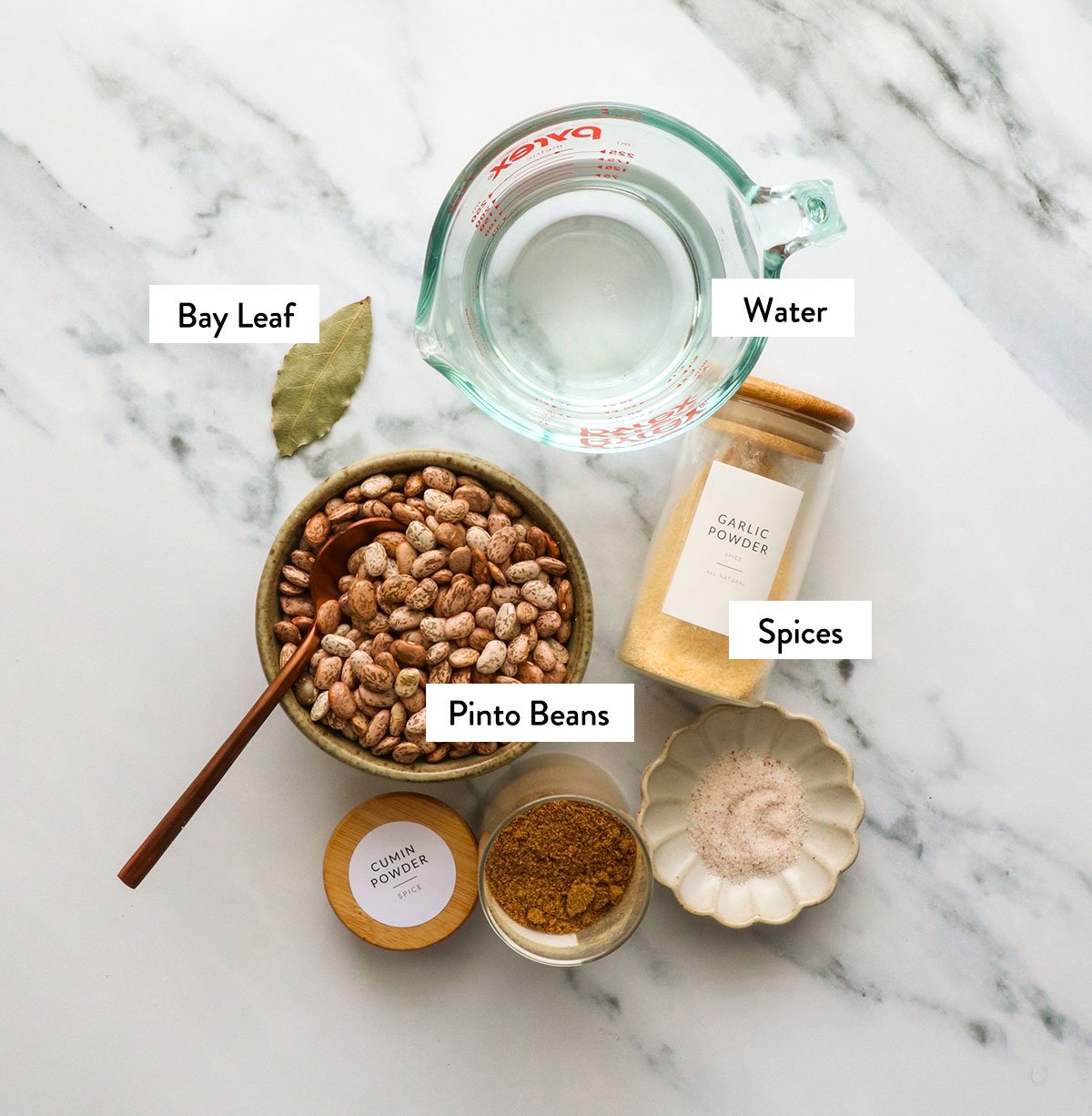 dry pinto beans, spices, and water labeled on a marble surface.
