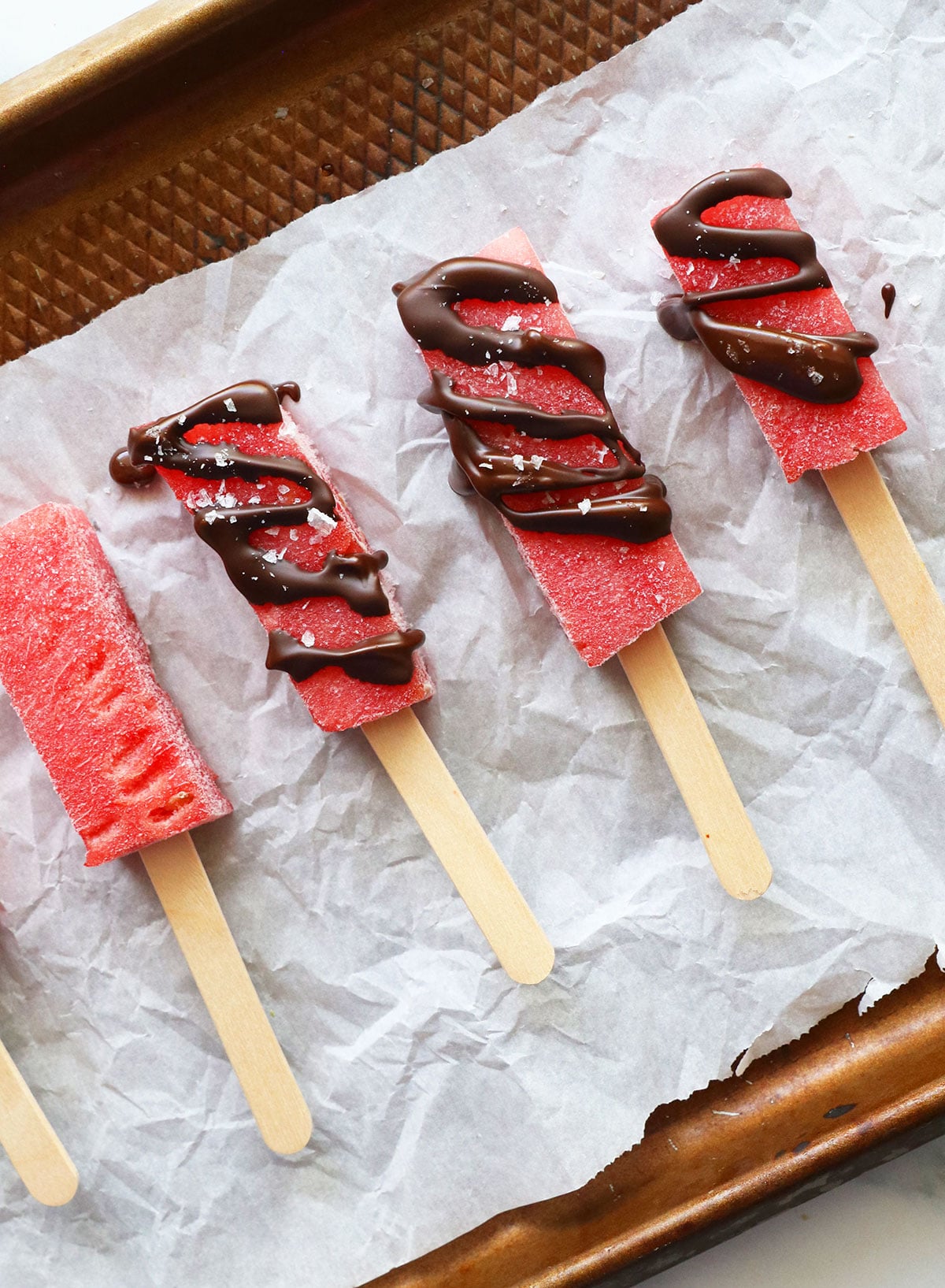 frozen watermelon pieces on a popsicle stick. Some pieces are drizzled with chocolate.