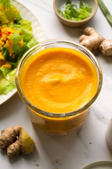 carrot ginger dressing in a glass jar near a salad.