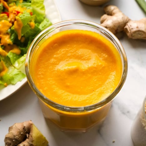 carrot ginger dressing in a glass jar near a salad.