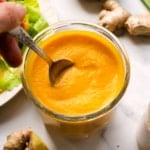 carrot ginger dressing in a glass jar stirred with a spoon.