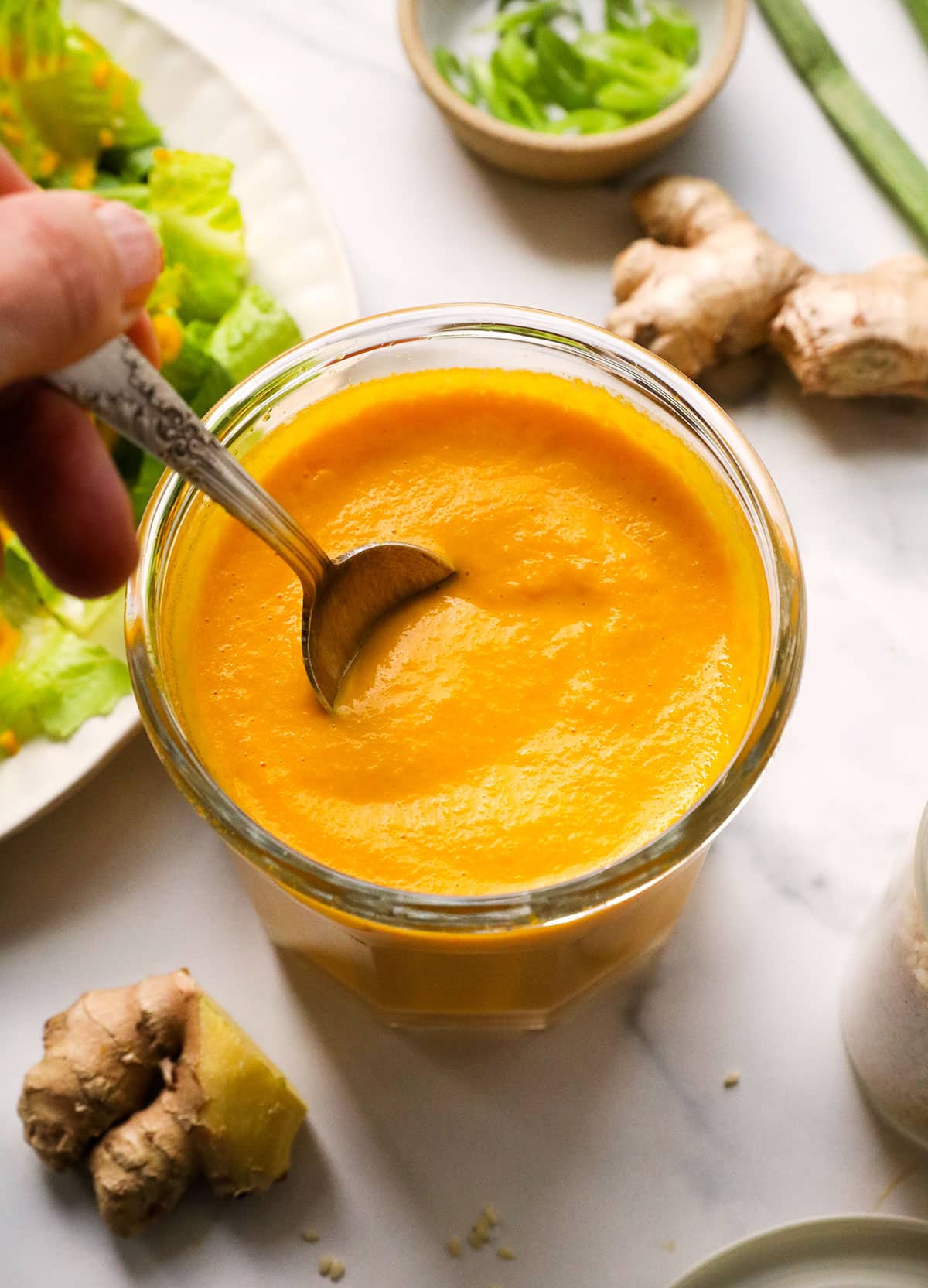 carrot ginger dressing in a glass jar stirred with a spoon.