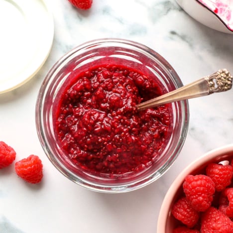 chia seed jam made with raspberries in a glass jar with a spoon.