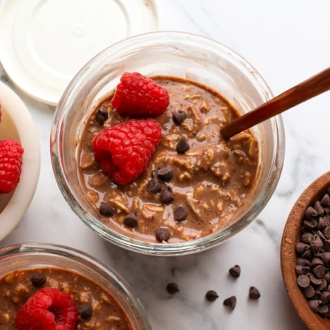 chocolate overnight oats in a glass jar with raspberries and mini chocolate chips.