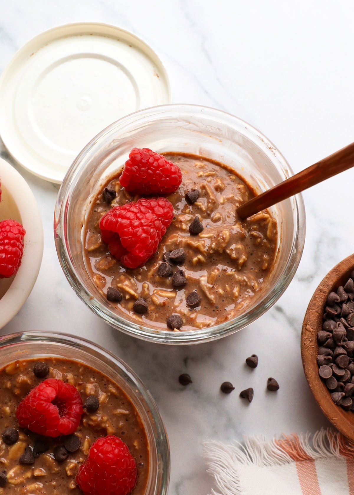 chocolate overnight oats in a glass jar with raspberries and mini chocolate chips. 