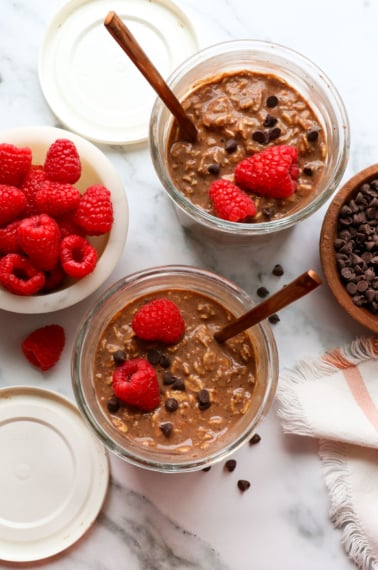 two jars of chocolate overnight oats topped with raspberries.