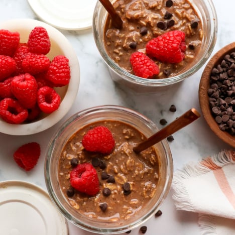 two jars of chocolate overnight oats topped with raspberries.