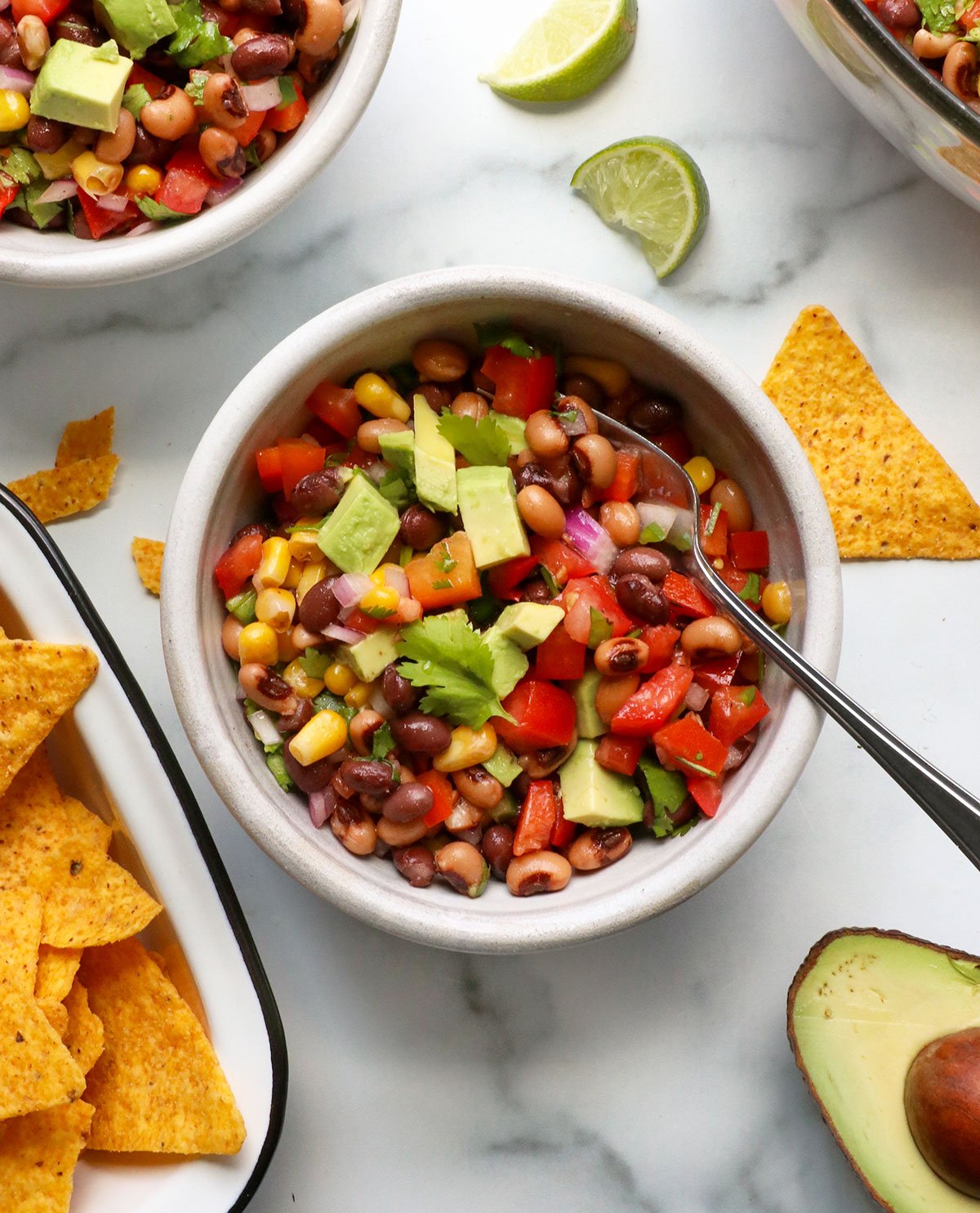 avocado added to bowl of cowboy caviar with a spoon.