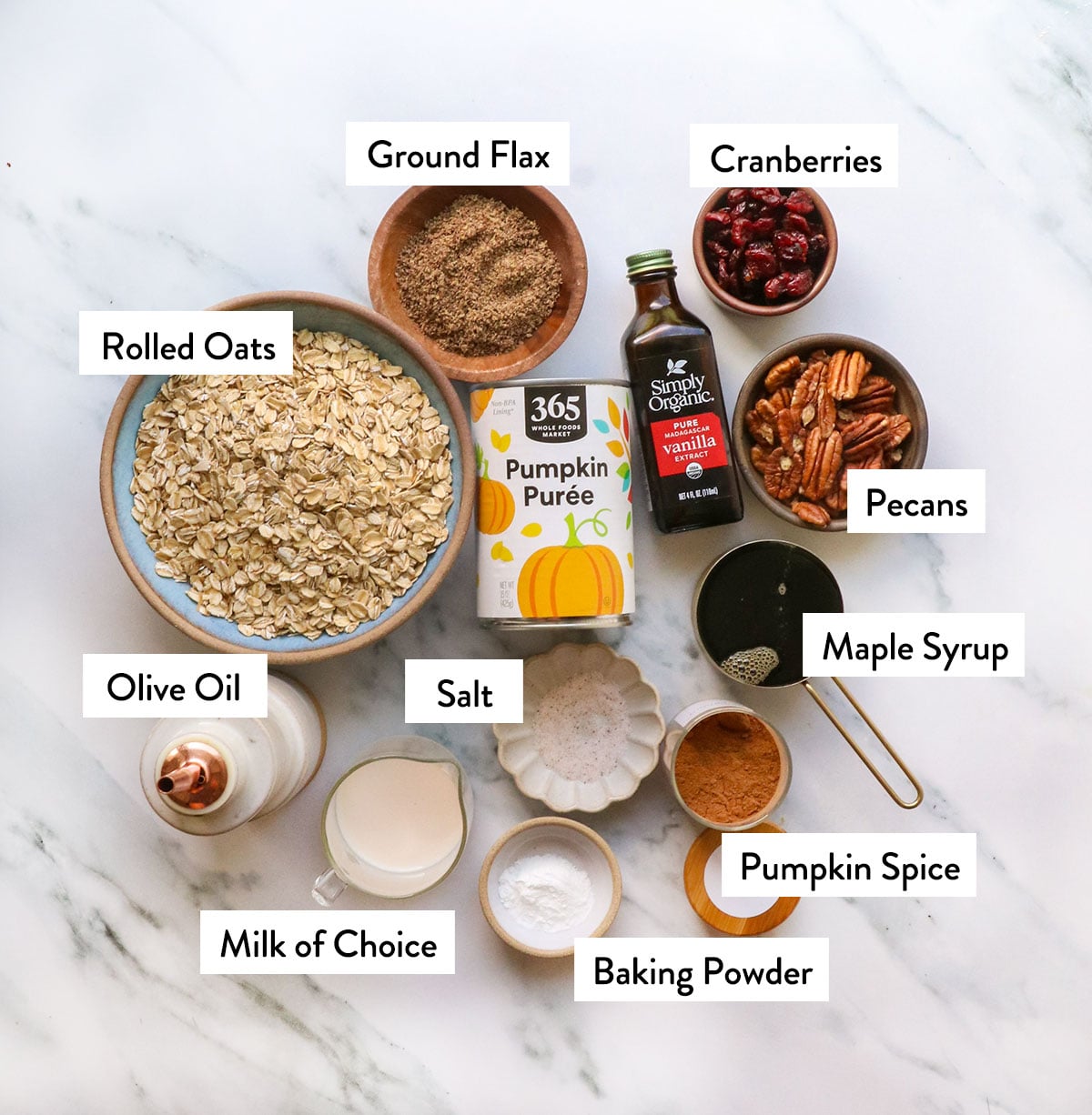 bowl of rolled oats, ground flax seed, pumpkin, maple syrup, and pecans on a white surface.