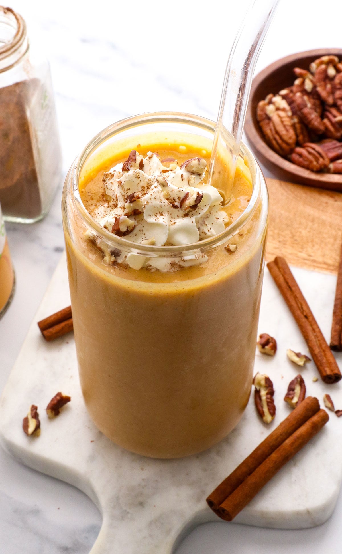 pumpkin smoothie in a tall glass with whipped cream and pecans on top.