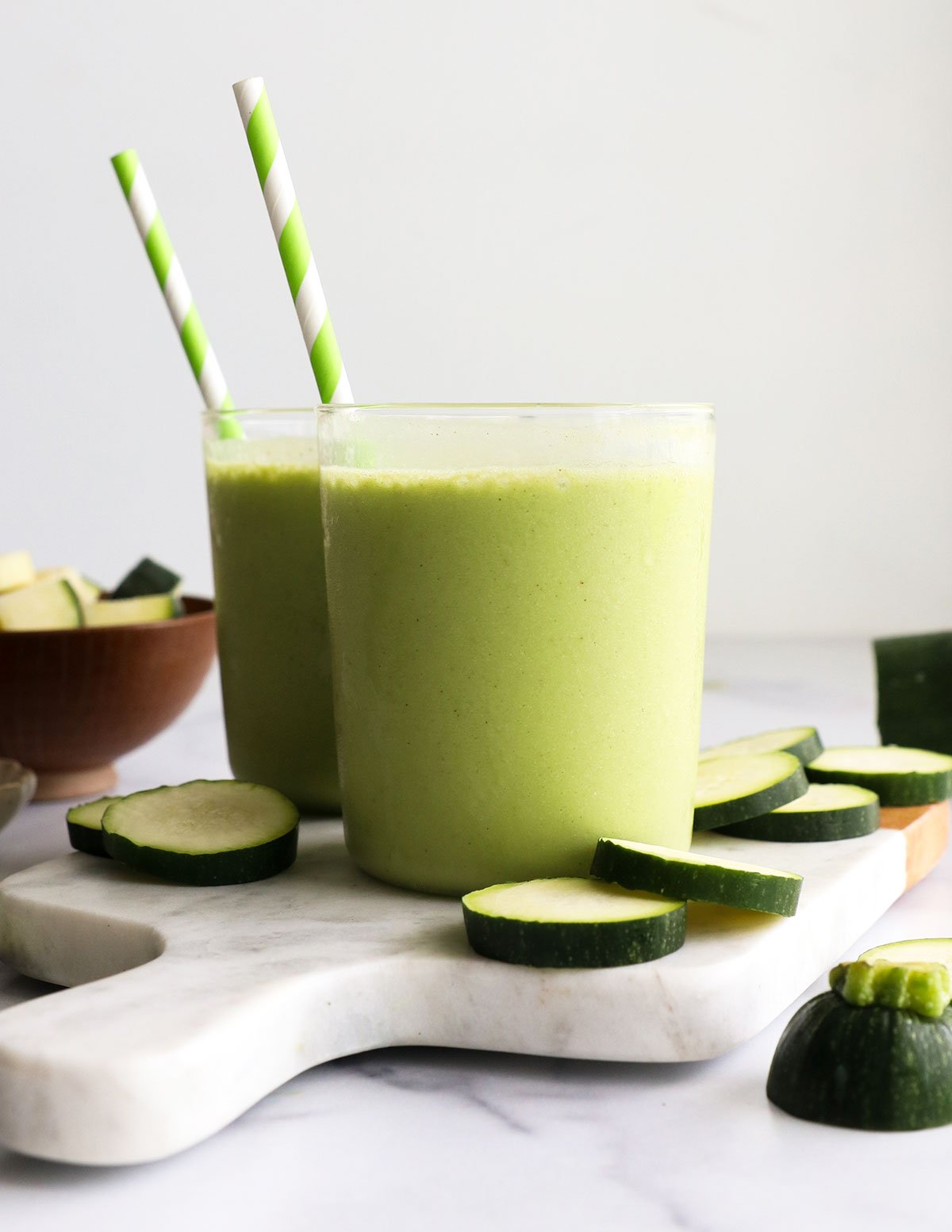 two glasses of zucchini smoothie with straws.