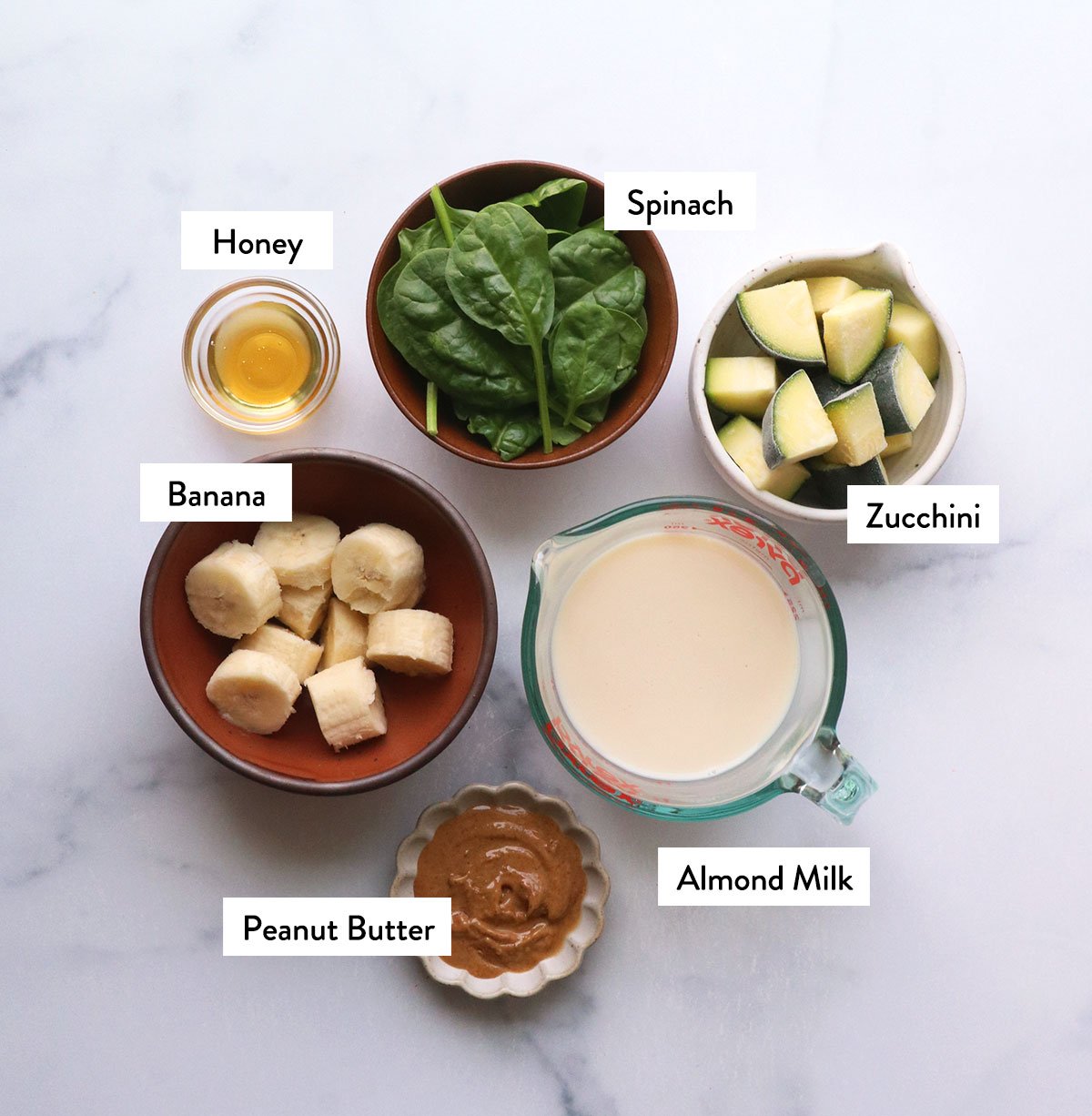 frozen zucchini and banana in bowls with spinch, milk, peanut butter and honey.
