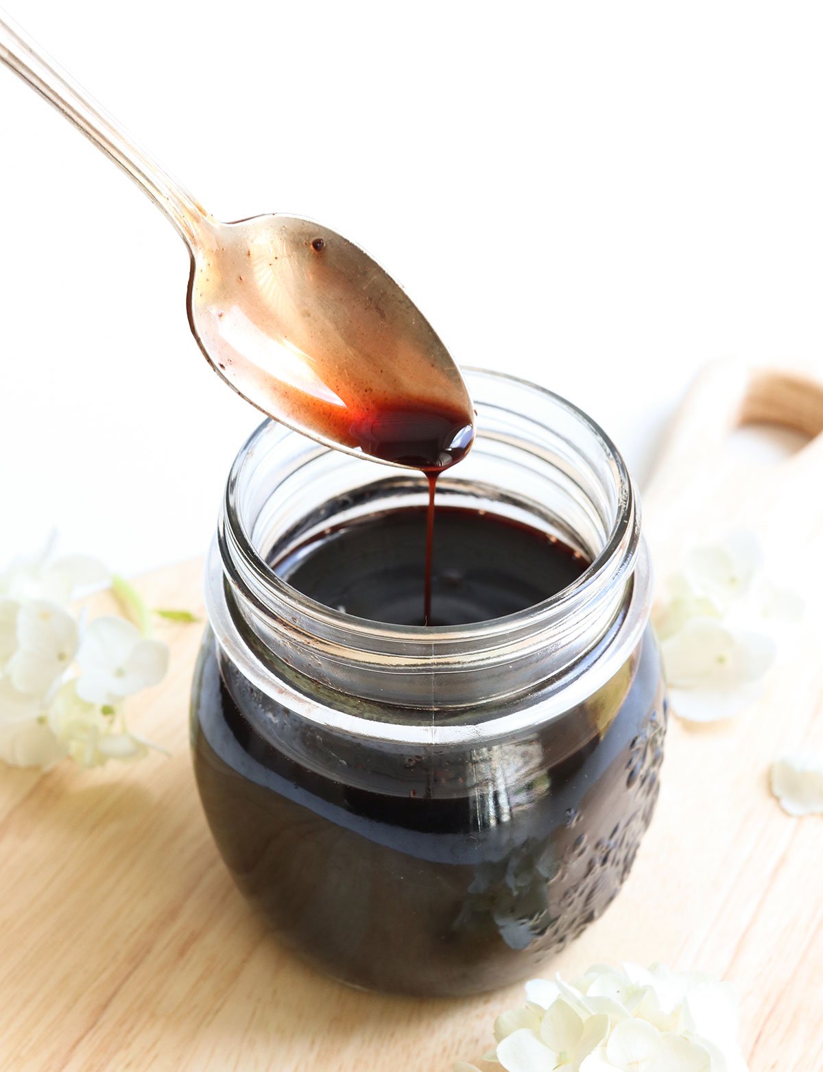 homemade elderberry syrup dripping off a spoon into a jar.