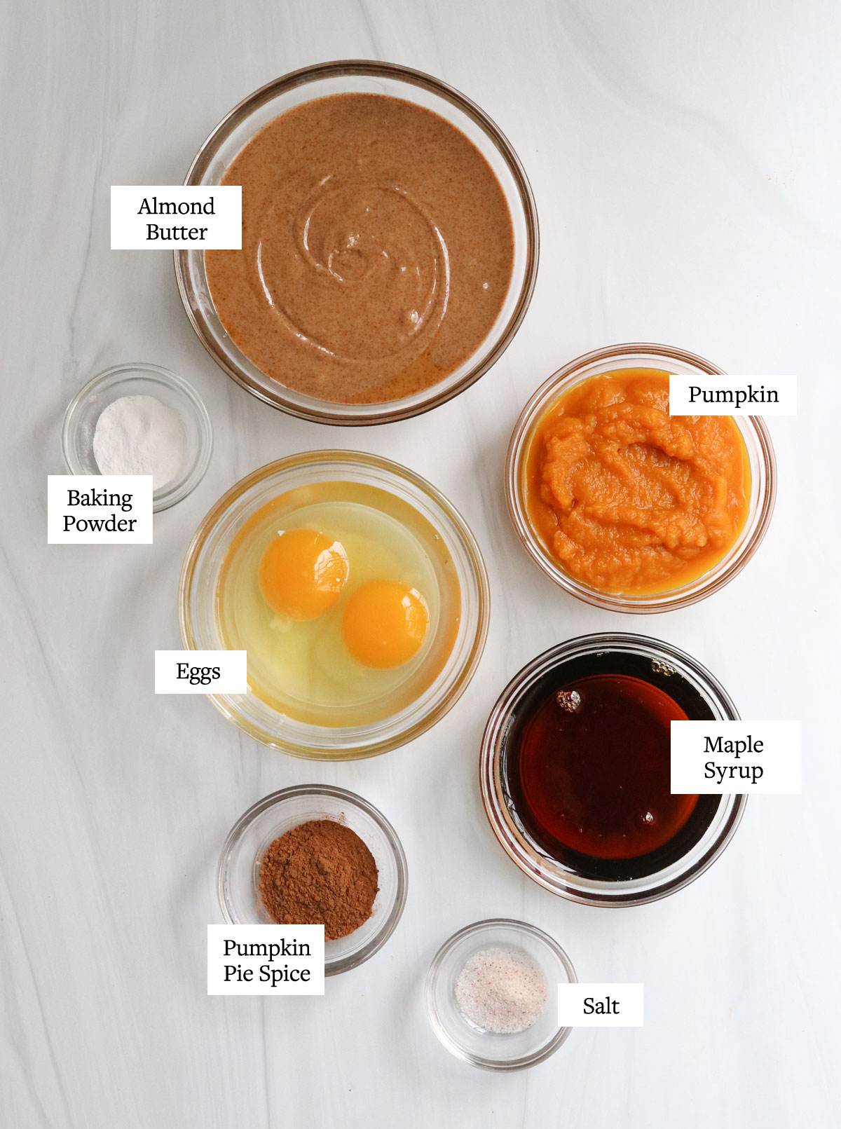 paleo pumpkin muffin ingredients in glass bowls on white table