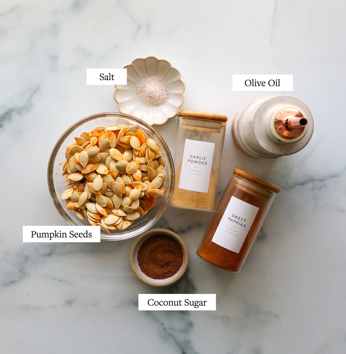 bowl of pumpkin seeds, spices, olive oil, and sugar on a white surface. 