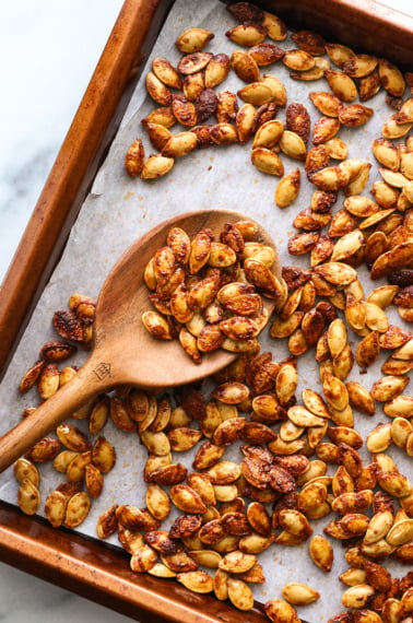 pumpkin seeds roasted on a lined pan with a wooden spoon.