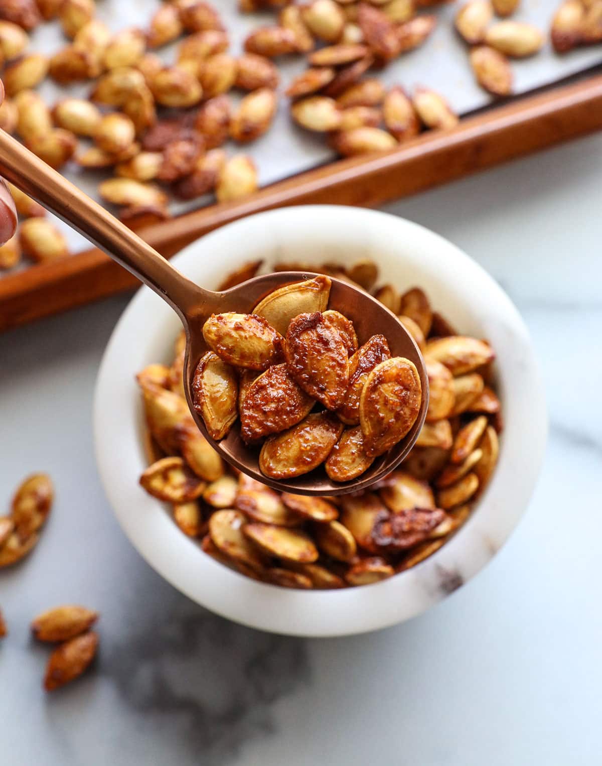 spoon lifting up roasted pumpkin seeds from a white bowl.