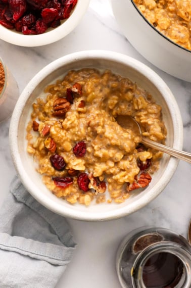 pumpkin oatmeal stirred with cranberries and pecans in a white bowl.